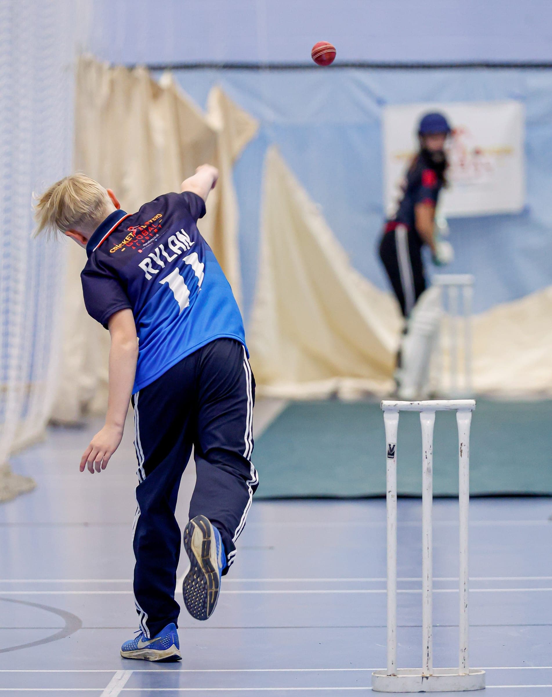 Boy bowling to a girl batter in indoor nets